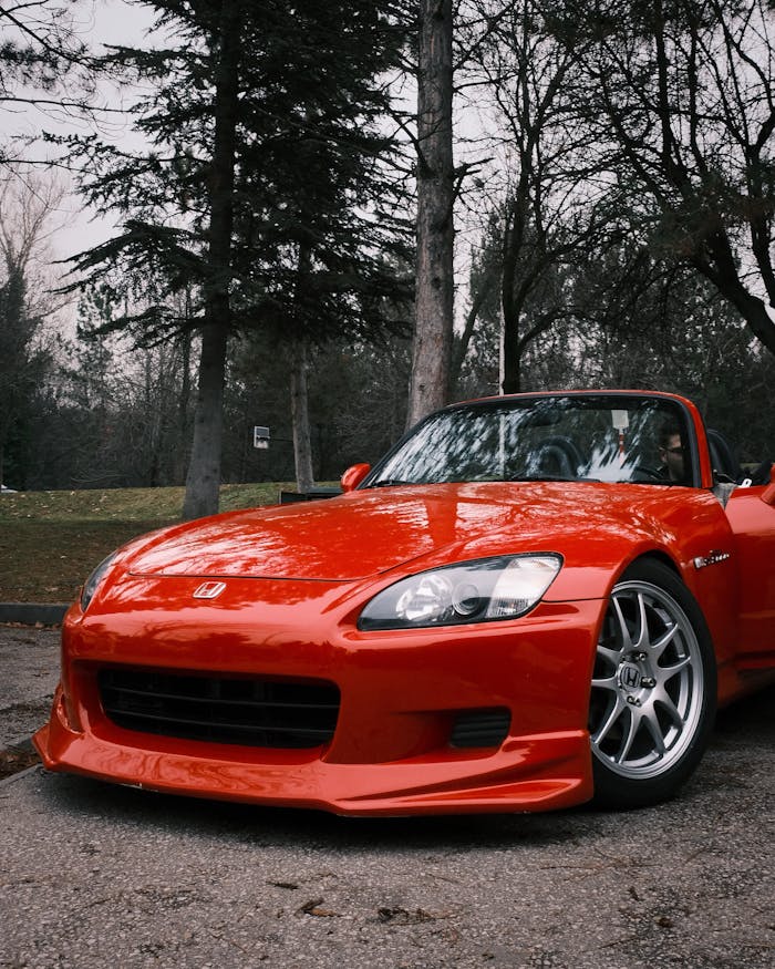A vibrant red convertible car parked in a wooded outdoor area.